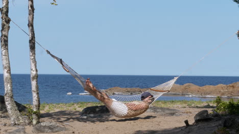 person sleeping on hammock and swinging in light breeze on ocean coastline