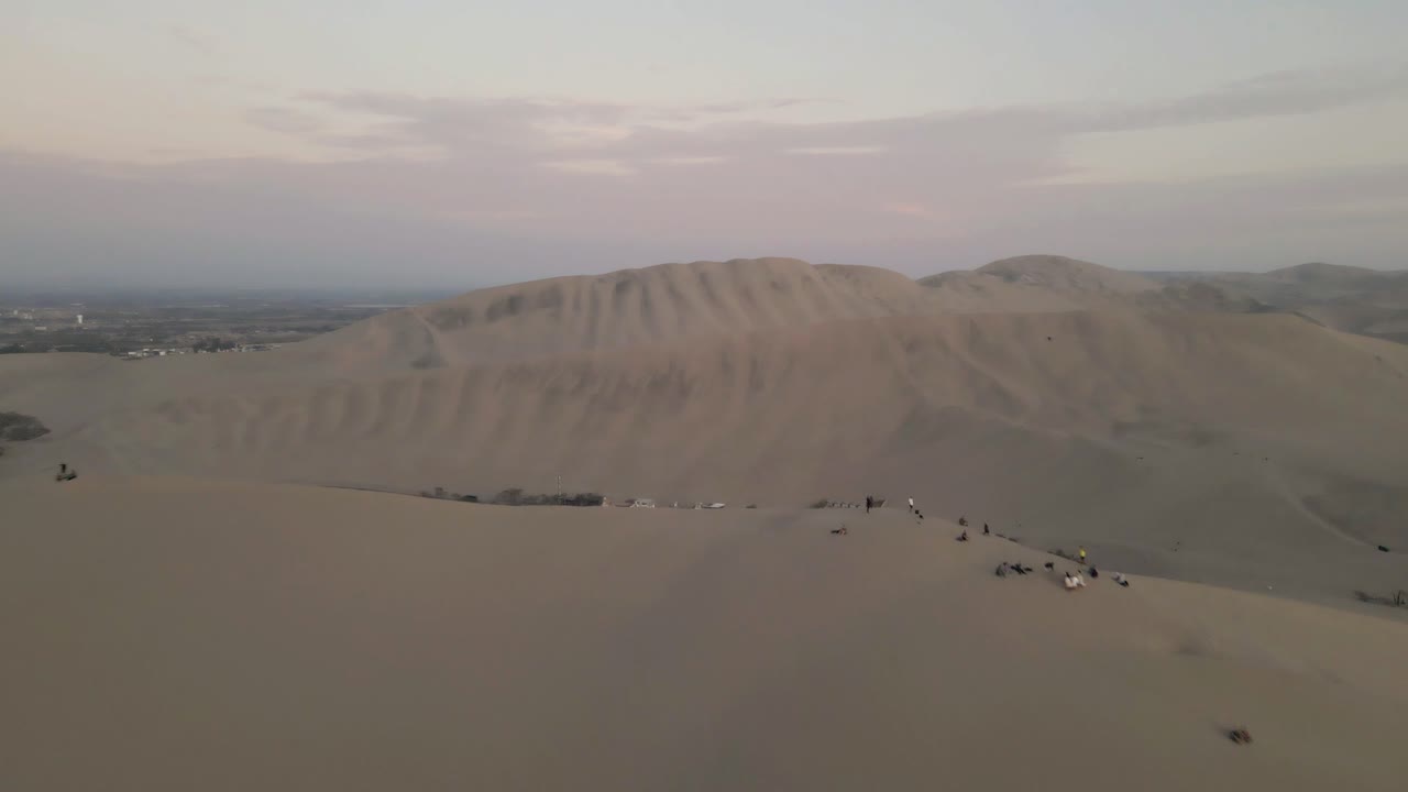 el dron se eleva con gracia sobre las dunas, pasa por la gente, revelando la joya del oasis, huacachina