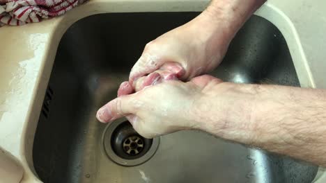 adult male cleaning hand palm and knuckles using soap at sink at home