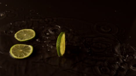 Lime-slices-dropping-on-wet-black-surface