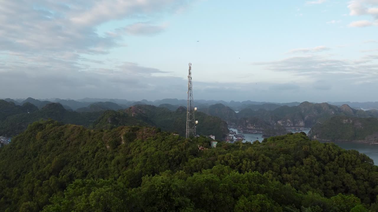 vista aérea hacia la torre de comunicaciones en la cima de una colina boscosa, la bahía de halong en el fondo, vietnam