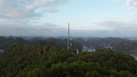 aerial view towards communication tower on forested hilltop, halong bay in background, vietnam