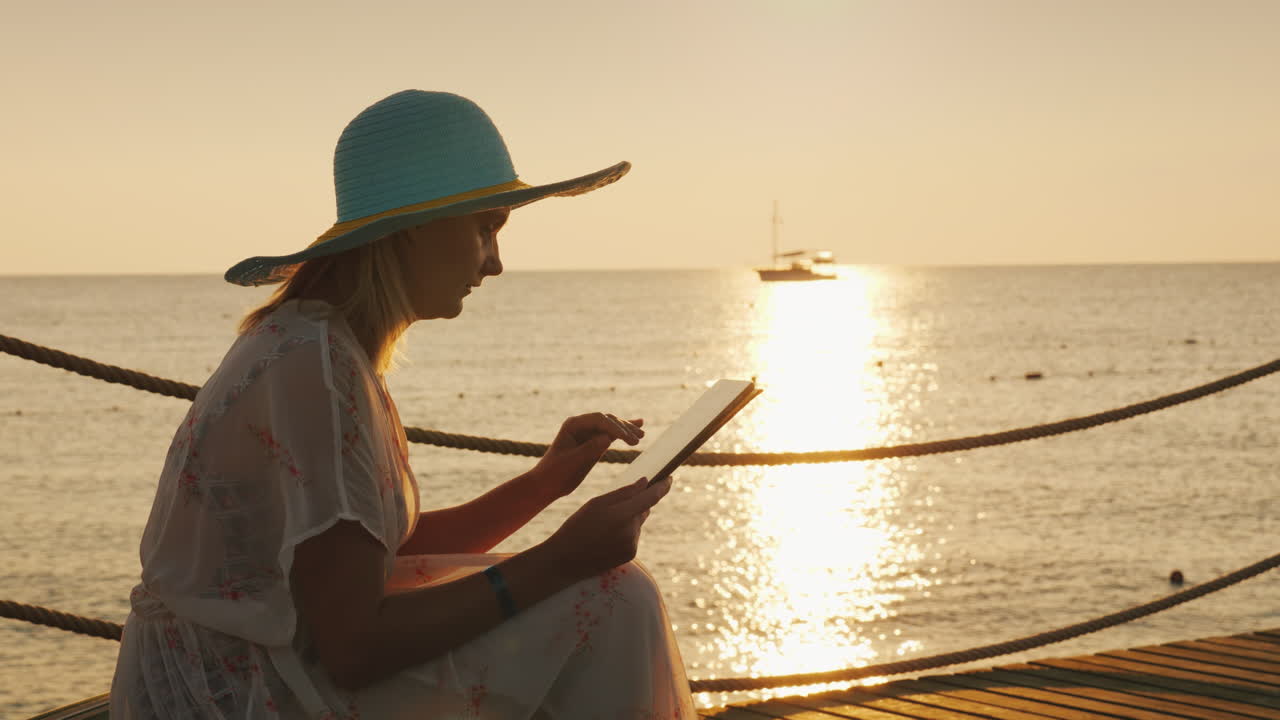 un turista con una tableta se sienta en el muelle pintoresco amanecer sobre el mar en el video de fondo 4k