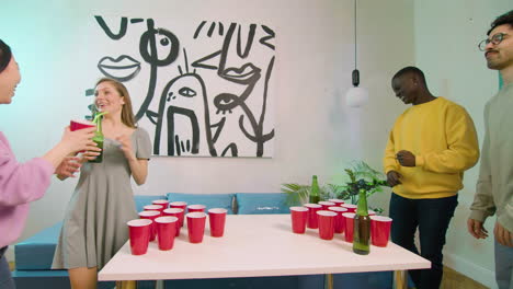 happy multiethnic young friends playing beer pong at home