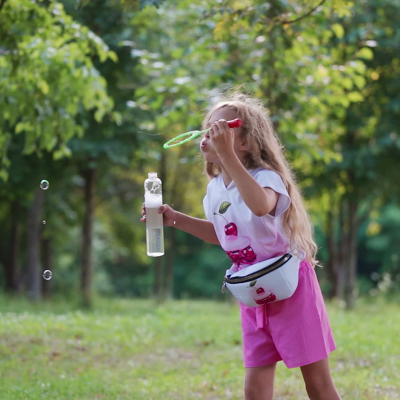 Little girl with bubble blower outdoors. Beautiful child blowing soap bubbles in the park. Happy girl with long hair blows shiny bubbles in the forest.