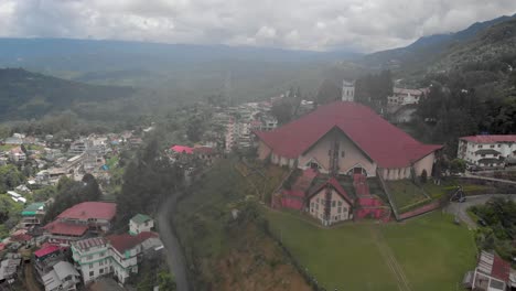 4k-Aerial-Spiral-shot-of-Kohima-Cathedral-built-in-Naga-Architecture-covered-in-Fog,-Nagaland,-India