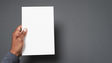 Video-of-hand-of-african-american-man-holding-book-with-blank-page,-copy-space-on-grey-background