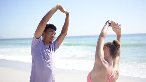 young biracial man and caucasian woman stretch on a sunny beach