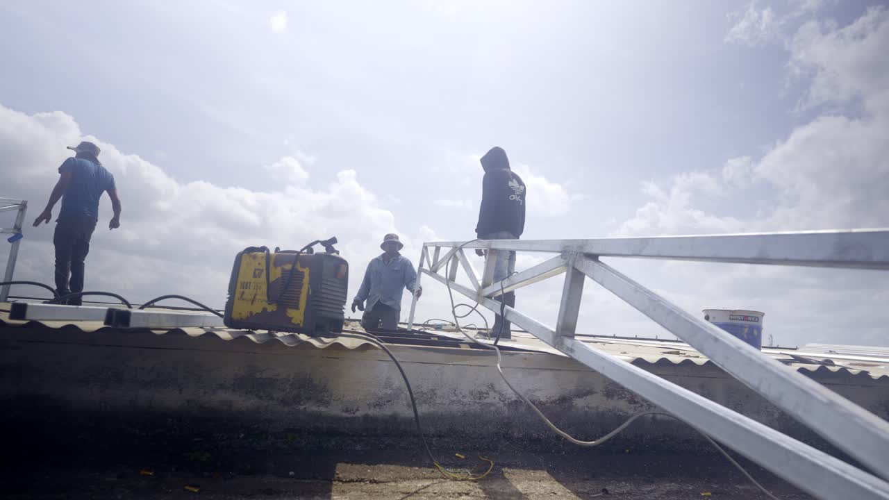 Three people working on roof of building, welding steel construction