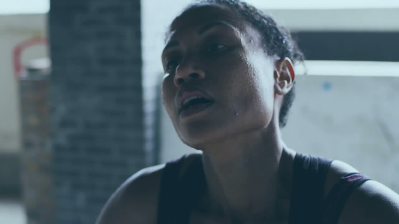 Female fitness trainee breathing after exertion in gym, highscore graphic appearing, obscuring face