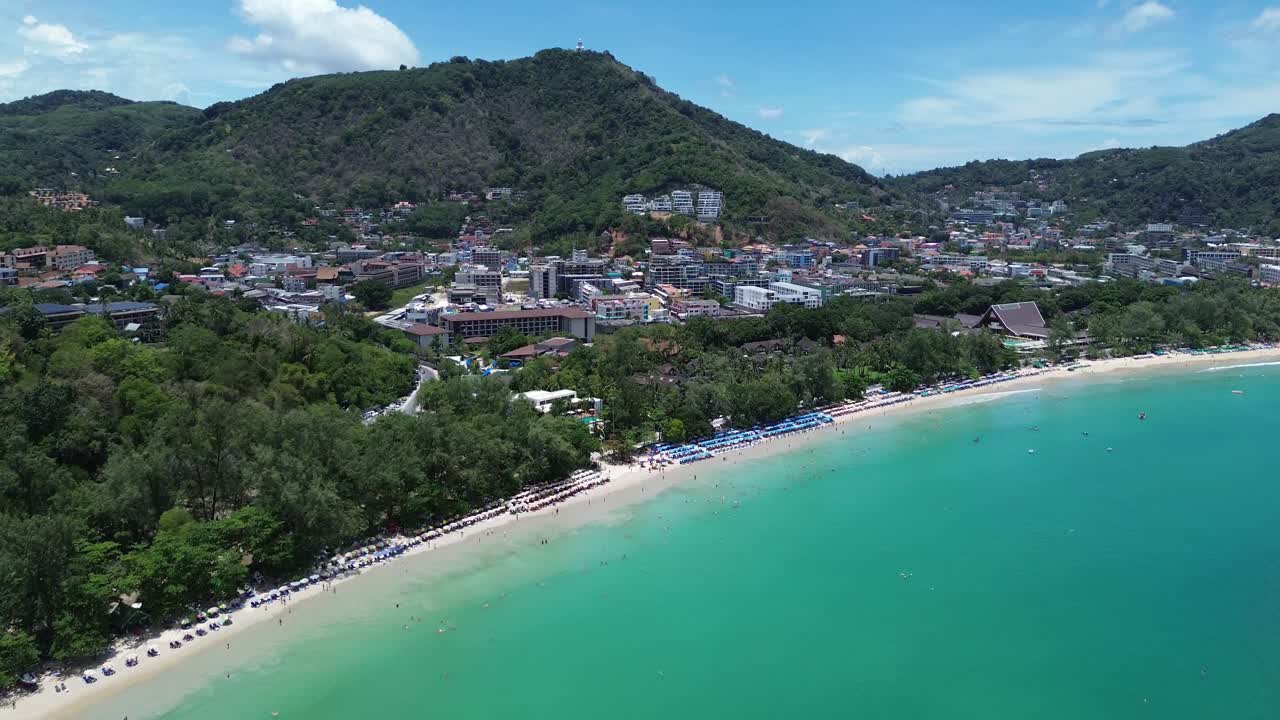 Drone zooms in revealing beach umbrellas and turquoise waters on a sunny day in Patong, Phuket
