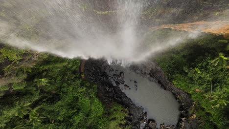 a unique close-up view of water pouring over a vertical cliff face into a natural rock pool below