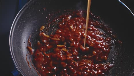 pouring broth into a frying pan with chopped onion and tomato sauce being cooked, close up view