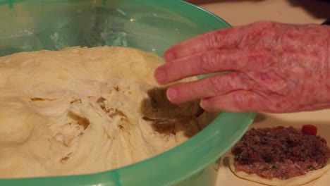 senior hands reaching for raw dough from inside a bowl