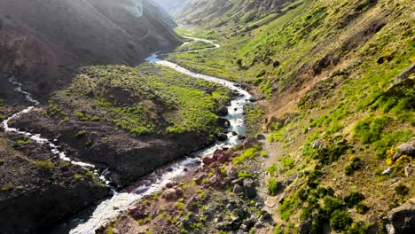 static aerial view of two men on horseback being followed by their dogs kicking up dust in the arid mountains and campanario river of maule, chile