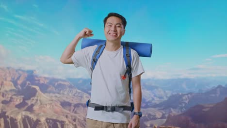 asian male hiker with mountaineering backpack smiling and flexing his bicep while traveling at the top of mountain