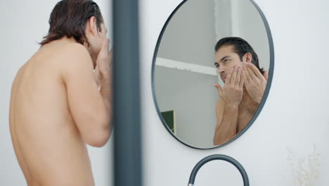 man applying skincare in bathroom mirror