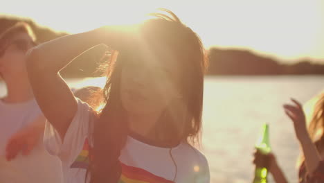 young girl with long dark hair in a short white t-shirt with a rainbow is dancing on the beach party with her friends. her hair is flying on the wind. she enjoys partytime with her eyes closed.