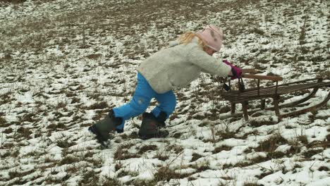 determined girl pushes sledge up a hill with lack of snow, slow motion