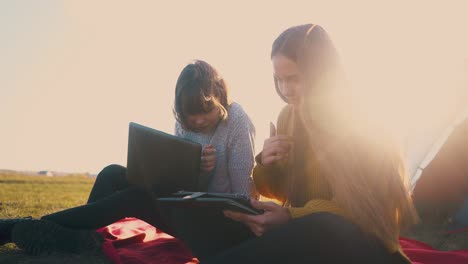 smiling women with tablet and laptop at tent against sunset