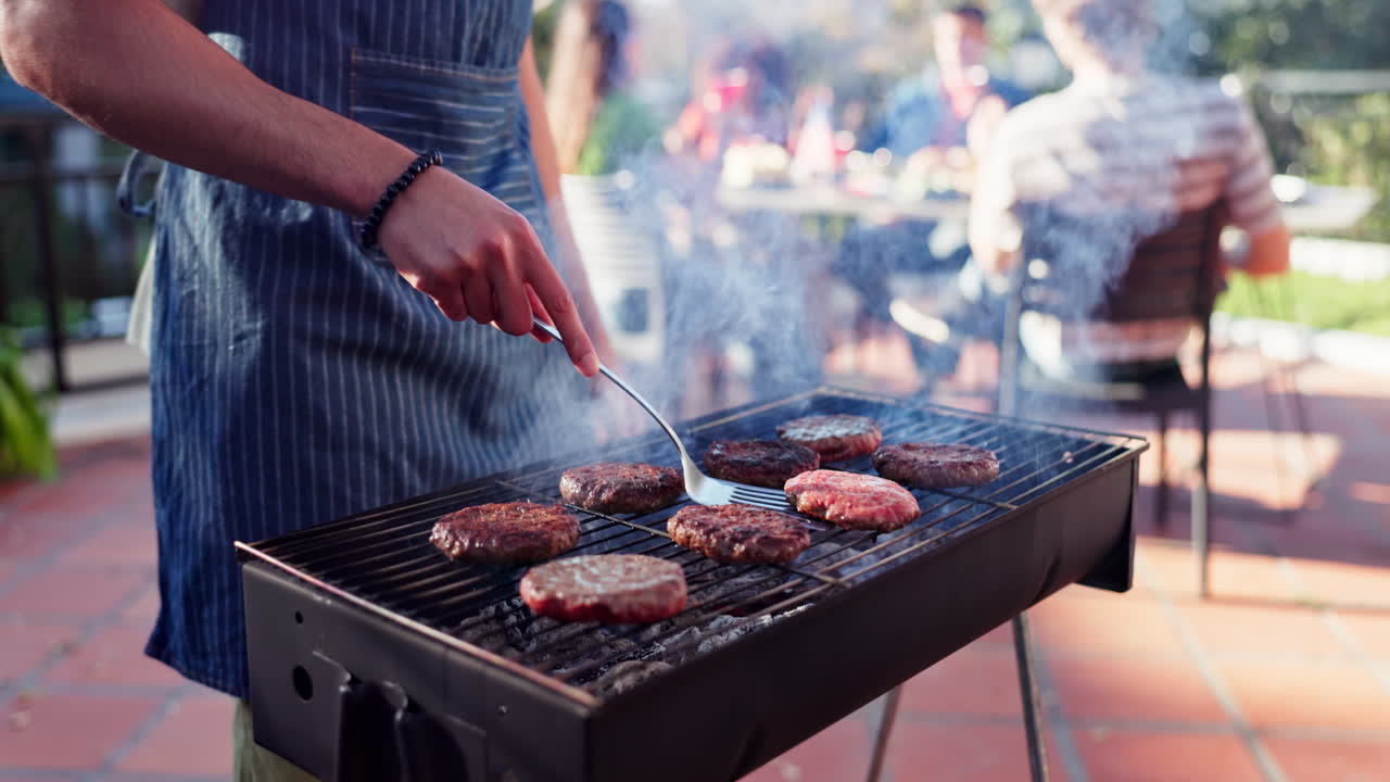 Burgers grilling on an outdoor barbecue with people in the background