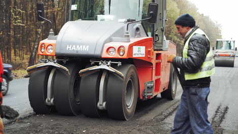 Workers in protective clothes with shovels working on the background of paver machines. New technics and team of workers making fresh asphalt. Street resurfacing.