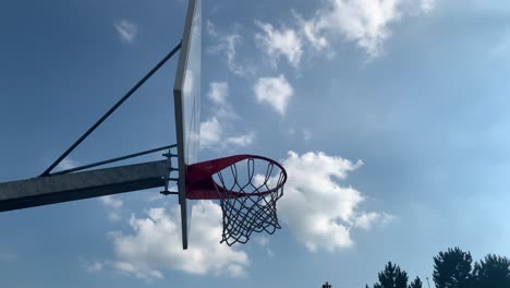 Pelota-De-Baloncesto-Entrando-En-El-Aro-Y-Cayendo-A-Través-De-La-Red,-Contra-El-Cielo-Azul