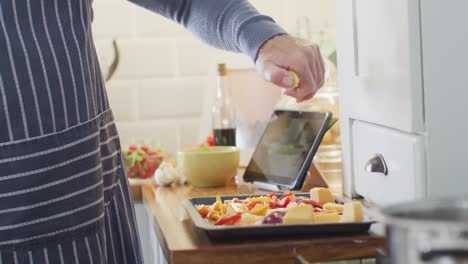 sección media de un hombre caucásico de pie en la cocina, cocinando la cena, aderezando la comida