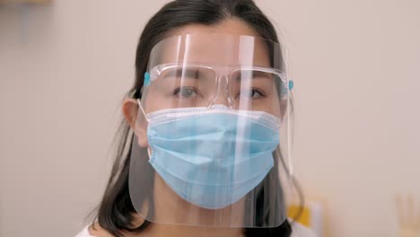 Portrait-of-an-Asia-young-female-who-is-wearing-a-face-shield-with-mask-rounded-around-her-face-from-a-frontal-perspective-to-protect-her-glasses-and-eyes,-scene-of-slow-motion