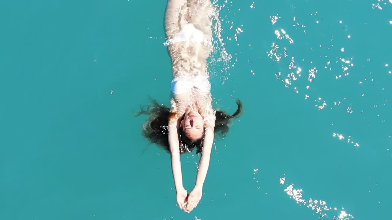 Caucasian woman in white swimsuit lying on green and transparent water. View from the top. Slow motion