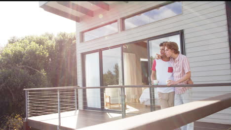 Happy-diverse-gay-male-couple-drinking-coffee-on-balcony-at-home,-slow-motion,-copy-space