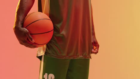 Video-of-midsection-of-african-american-male-basketball-player-holding-ball-on-orange-background