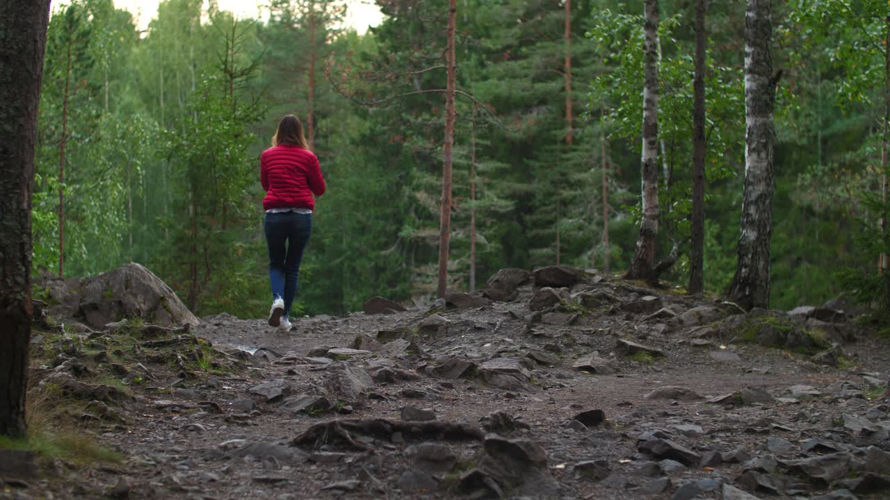 Woman in red jacket and blue jeans walking on Karelian rocks with moss and plants in 4k 50 fps, slow motion