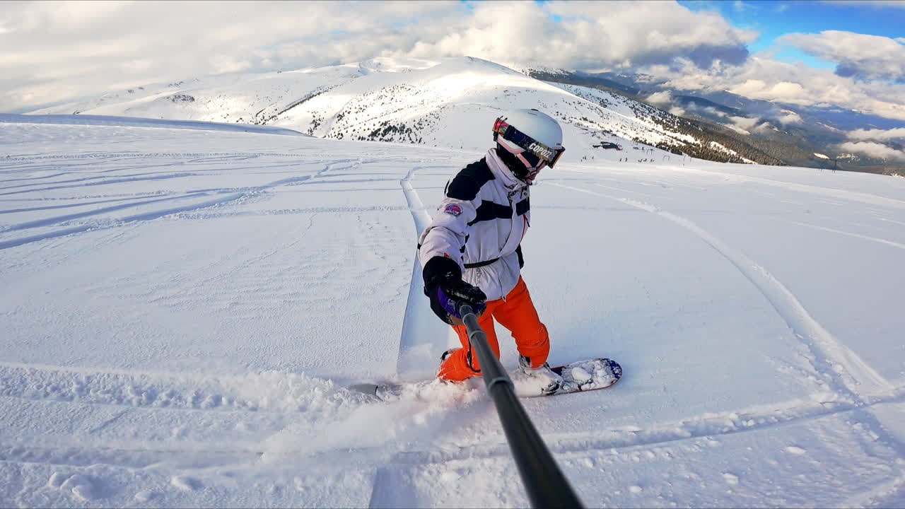 Taking selfie of a snowboard ride. Snowboarder goes by the beautiful landscape and gestures to camera.