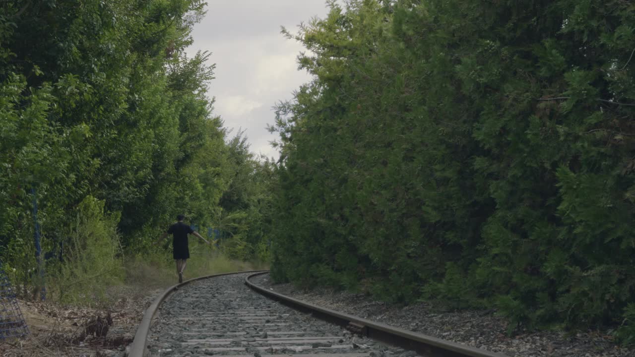 A man walks along abandoned railway tracks in the middle of a lush green forest, balancing carefully as he enjoys nature and the peaceful atmosphere. A serene and joyful moment representing freedom