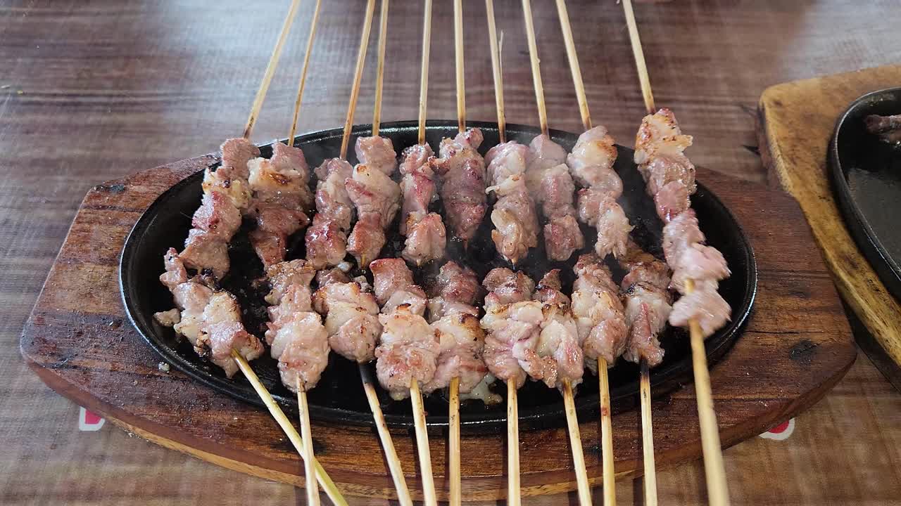 satay de cabra fresco cocinando en una placa de calor, la persona gira los pinchos, de cerca