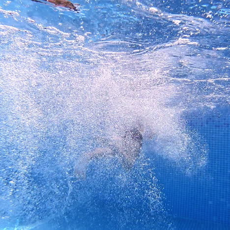 Underwater view with splash bubbles. Man jumps into the blue water in the swimming pool. Concept of sport, swimming pool, fitness.