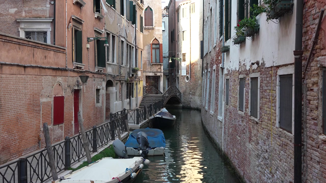 Peaceful view of a narrow Venice canal lined with historic buildings, moored boats, and a small stone bridge in the heart of Venice, Italy