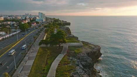 aerial flight along coastline of santo domingo with traffic at maritimo promenade during sunset time - establishing drone shot