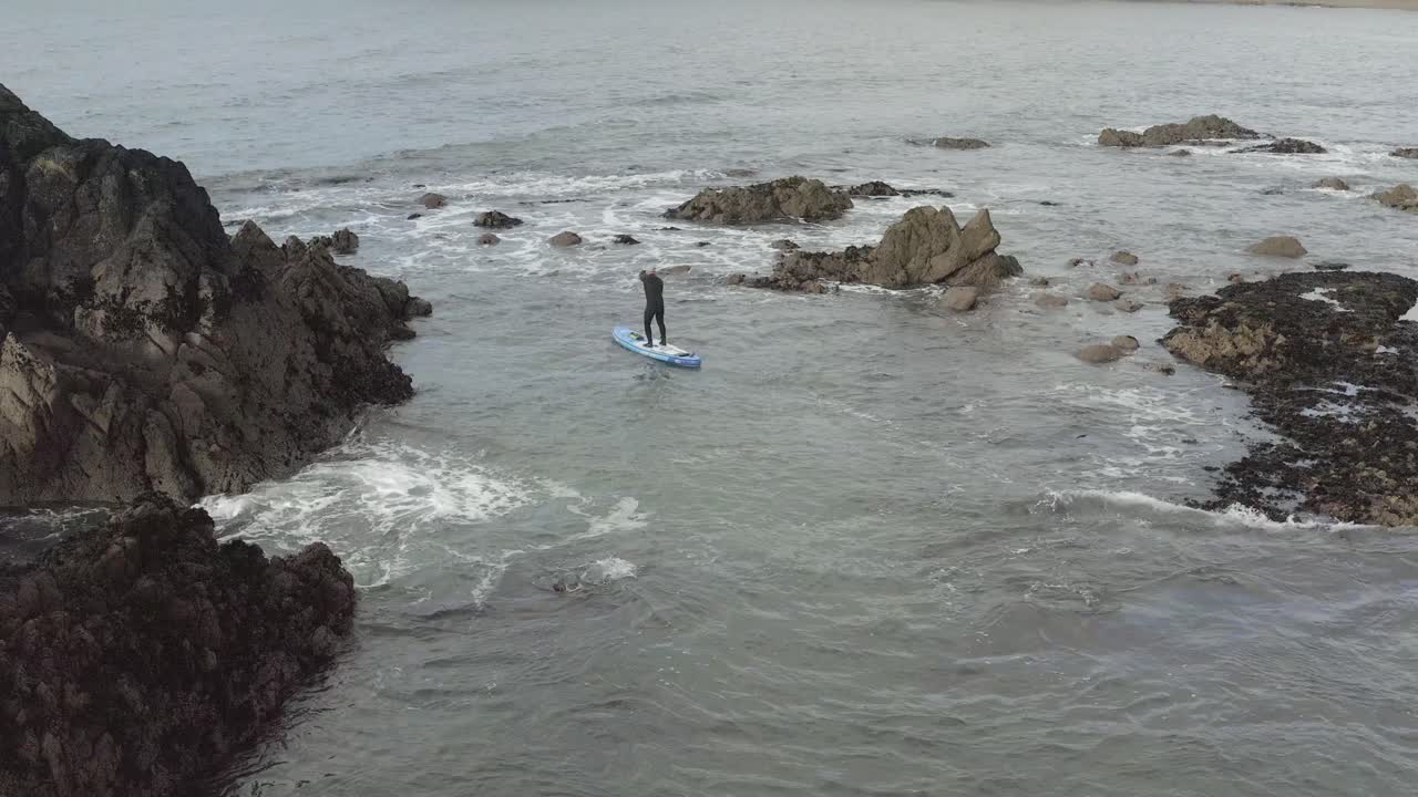 paddleboarder en traje de neopreno en aguas caóticas alrededor de los islotes oceánicos durante la marea baja.