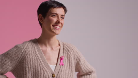 retrato de estudio de una joven sonriente que lleva una cinta rosa de concienciación sobre el cáncer de mama contra un fondo rosa 1