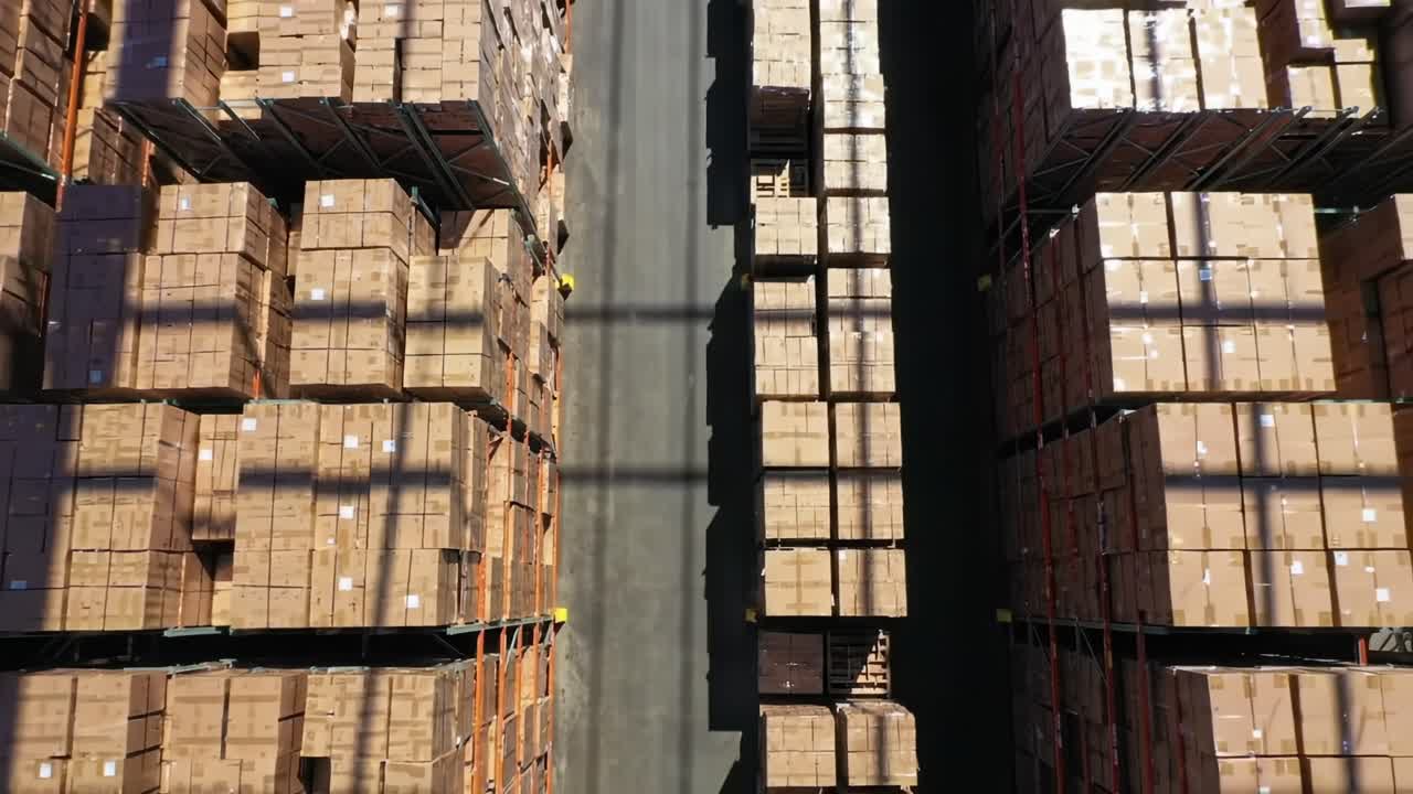 A high-angle view of a bustling warehouse shows rows of neatly stacked boxes ready for distribution. Forklifts are seen moving around as workers manage inventory and shipments.