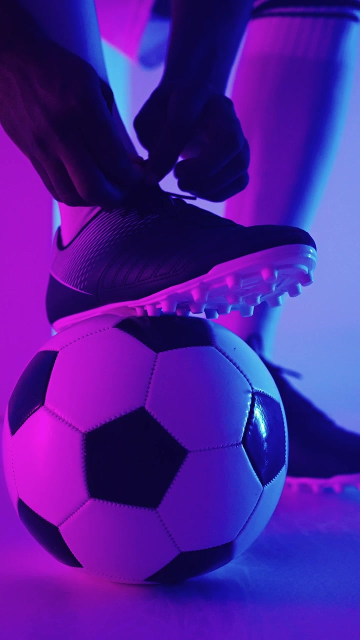 Neon ışıklar altında, ayağı topun üzerindeyken kramponlarını bağlayan futbolcu