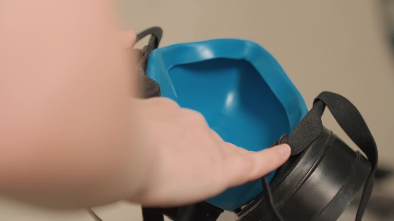 Donna caucasica che lava la superficie interna del respiratore con acqua e sapone, primi piani focalizzati delle punte delle dita che risciacquano l'area della cartuccia, delicata strofinatura e preparazione all'asciugatura per la sanificazione domestica vicino al lavello.