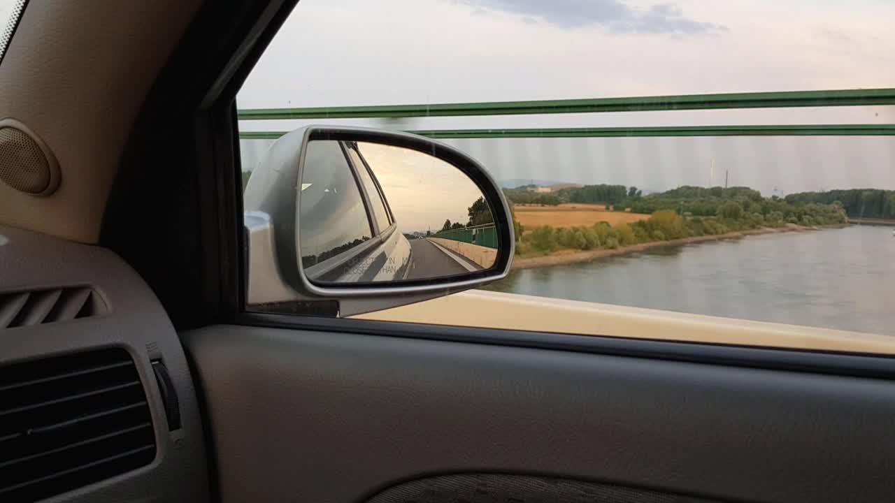 Looking into rear view mirror while driving over water on a bridge in Germany.