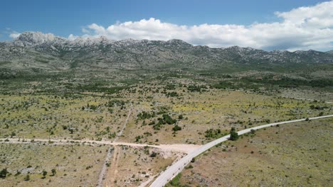 Arid-karst-region-of-Velebit-mountain-in-Zadar-county-in-summer,-the-view-from-above-over-road-and-filed-with-horizon-blocked-with-mountain-range