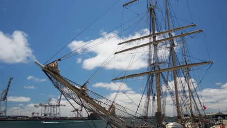 tall ship moored against a dock with commercial harbour in the background