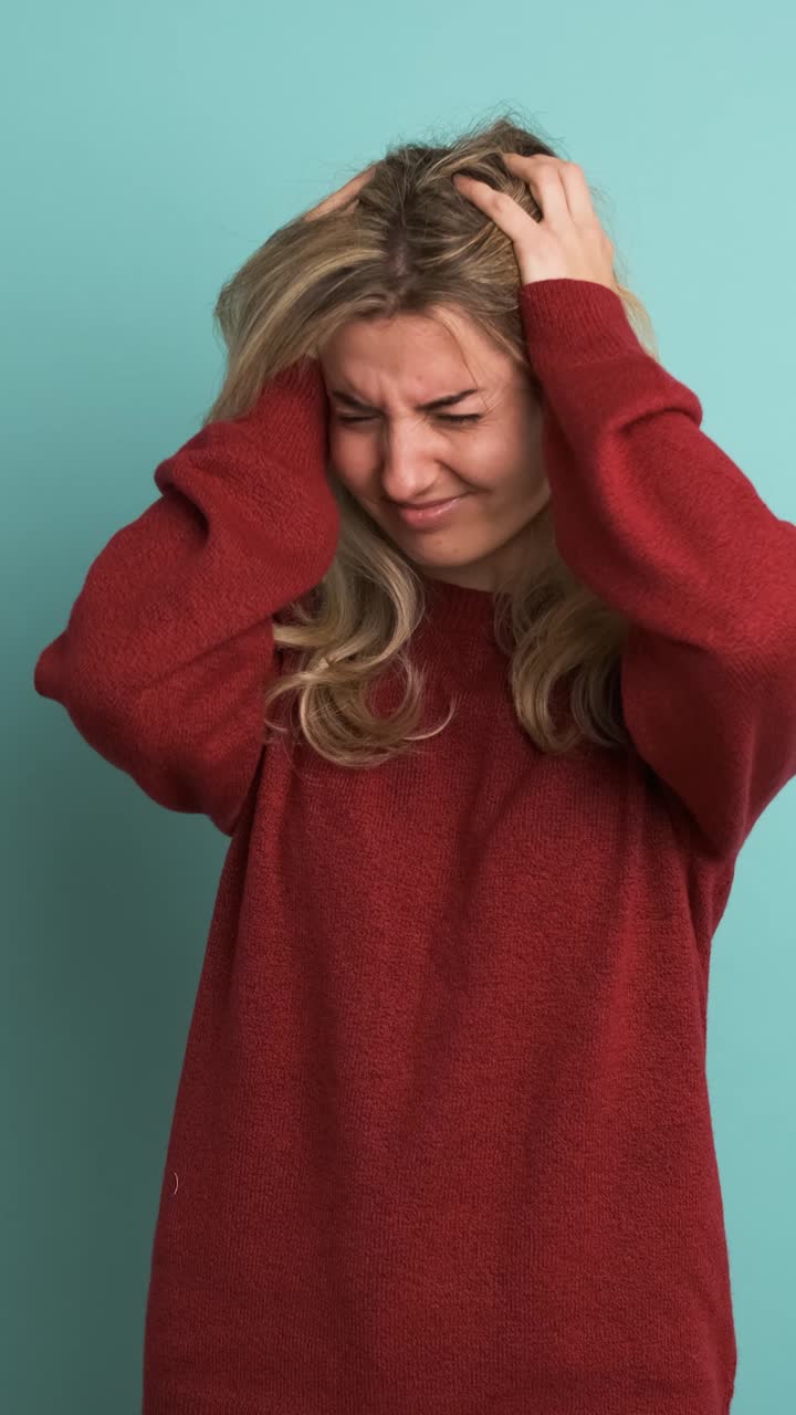 Frustrated woman suffering from headache in blue studio