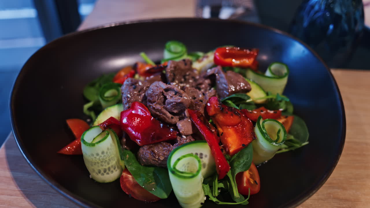 Close up of a salad with meat and vegetables on a black plate at a restaurant