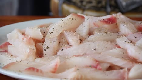 raw white fish on a white plate being seasoned with salt and pepper in slow motion with slider moving sideways